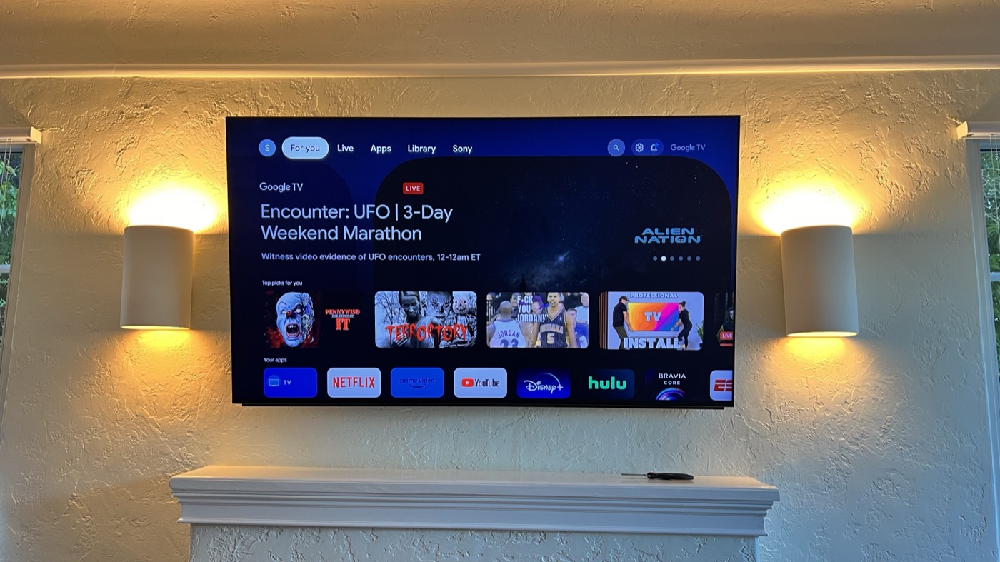 Television mounted above a fireplace between two wall sconces